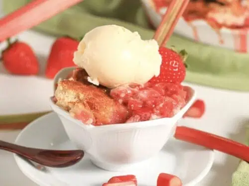 strawberry rhubarb dump cake serving in a bowl on a saucer, topped with ice cream.